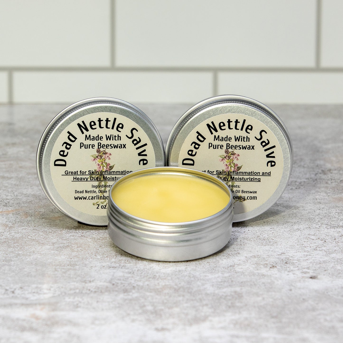 Two tins of Dead Nettle Salve on a gray surface with a tiled wall background.
