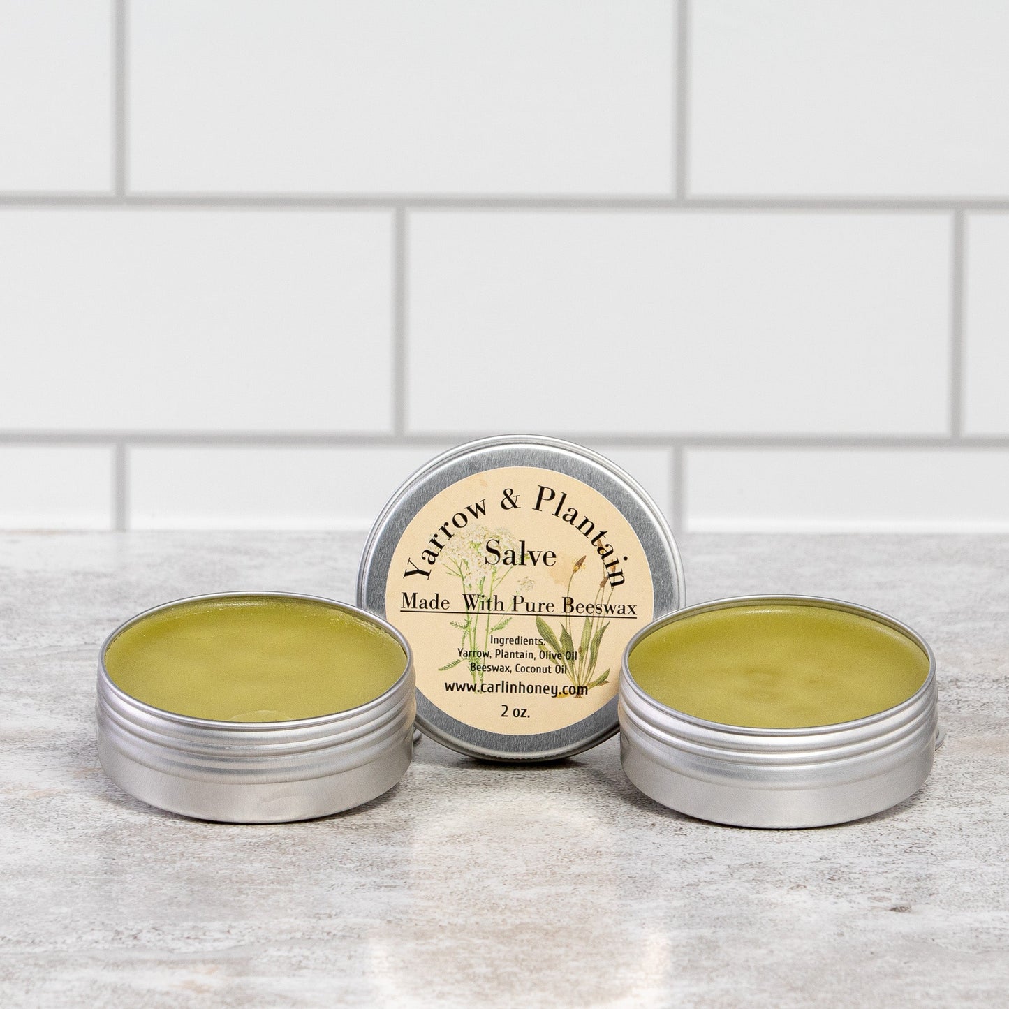 Three tins of salve on a wooden surface with a white tiled wall background