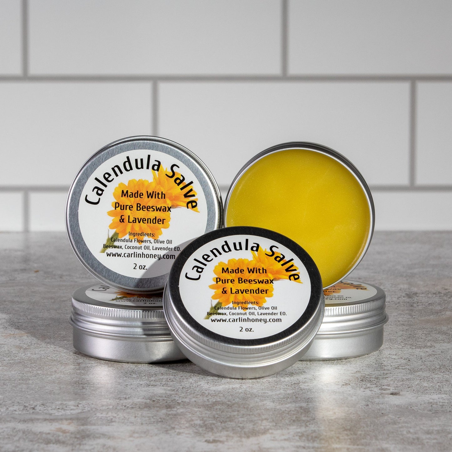 Calendula salve tins with labels on a gray surface against a tiled wall background