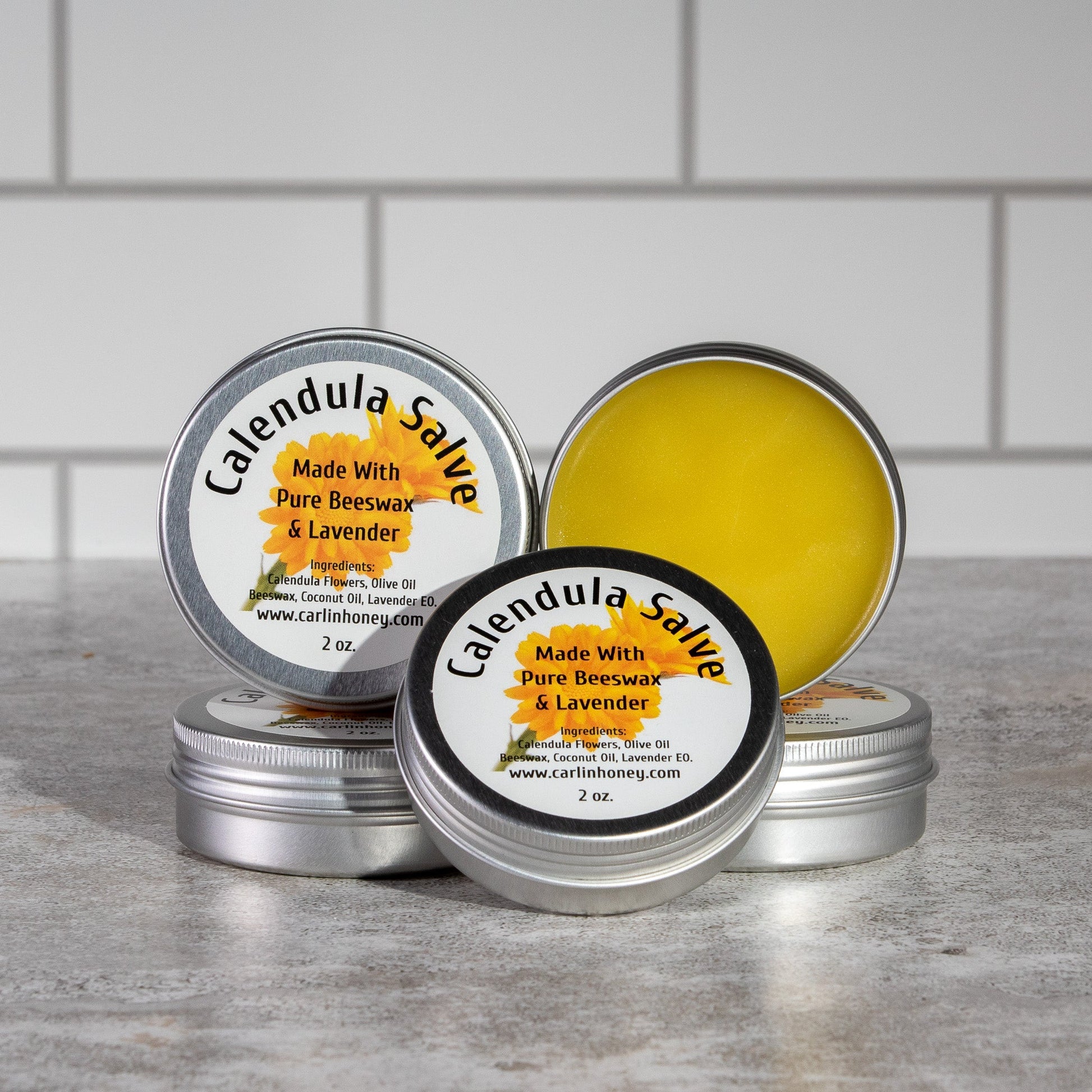 Calendula salve tins with labels on a gray surface against a tiled wall background