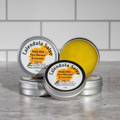 Calendula salve tins with labels on a gray surface against a tiled wall background