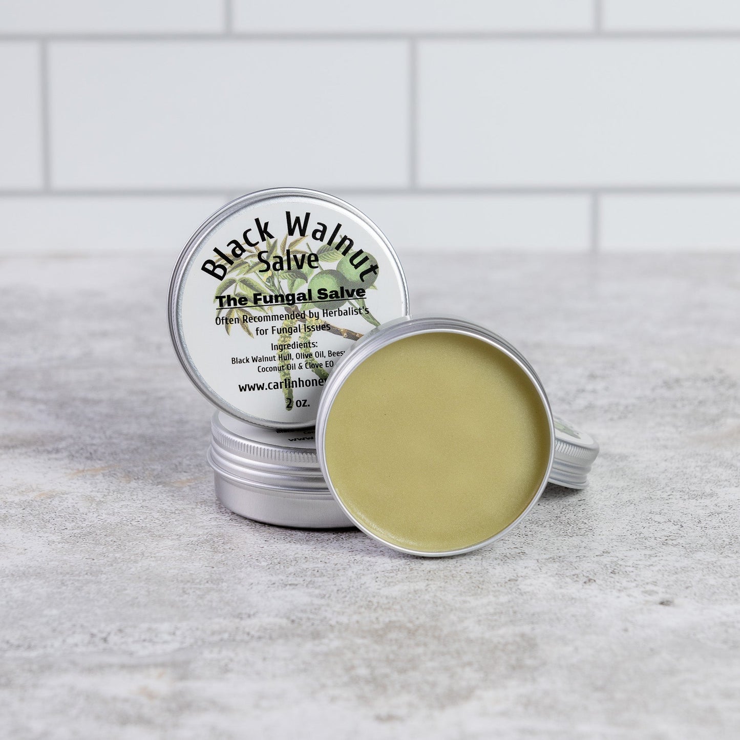 Two tins of Black Walnut Salve on a gray surface with a white tiled background