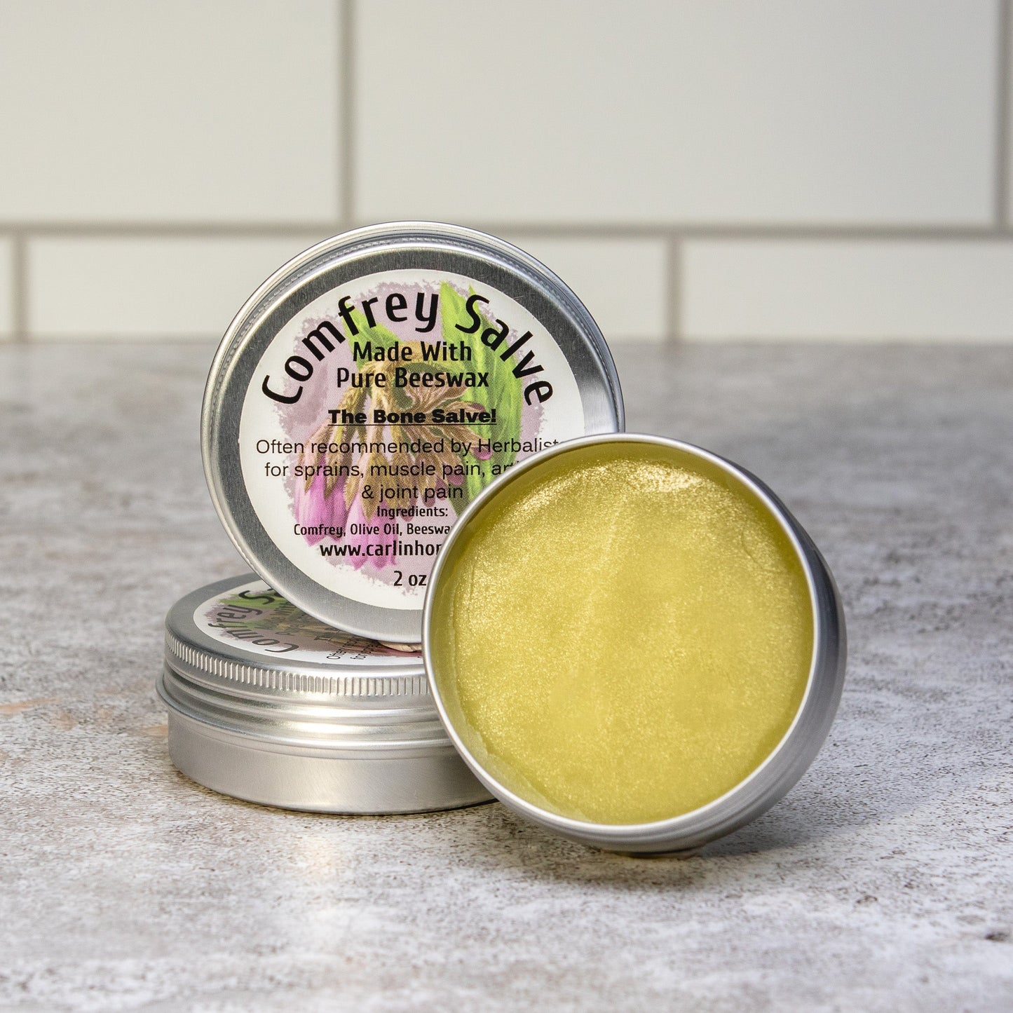 Comfrey salve in a metal tin on a countertop with a white tiled wall background