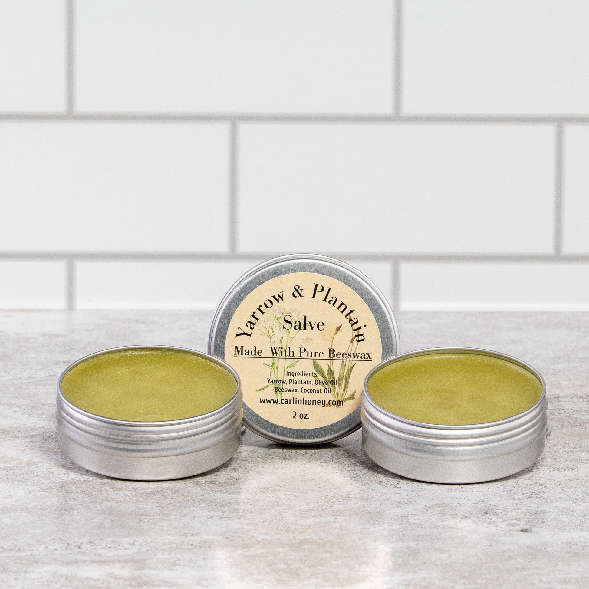 Three tins of salve on a wooden surface with a white tiled wall background