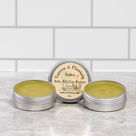 Three tins of salve on a wooden surface with a white tiled wall background
